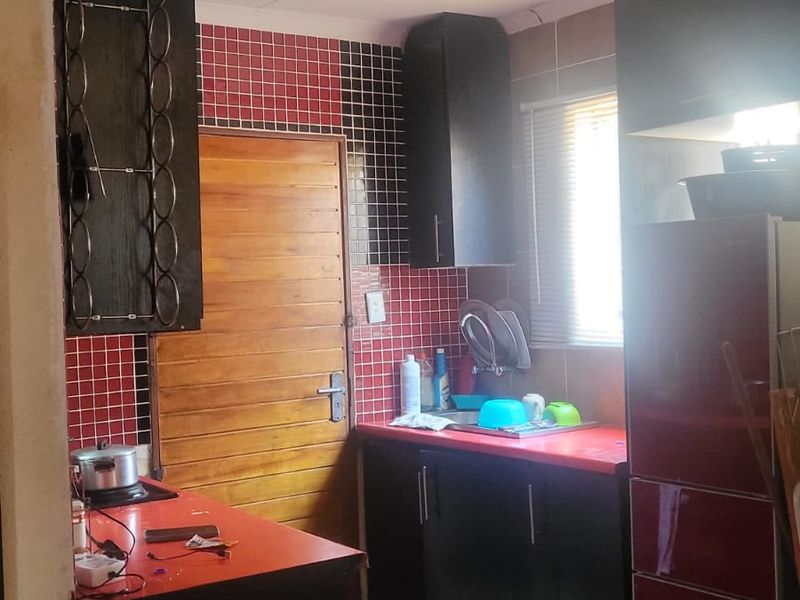 A compact kitchen featuring dark cabinetry, red countertops, a tiled backsplash, and tiled flooring, providing a functional workspace with natural light.