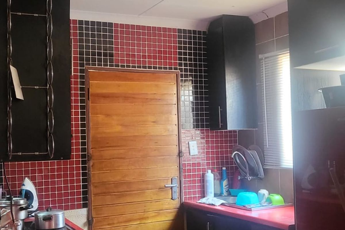 A compact kitchen featuring black cabinetry, red countertops, and a distinctive red and black tiled backsplash with integrated sink and hob.