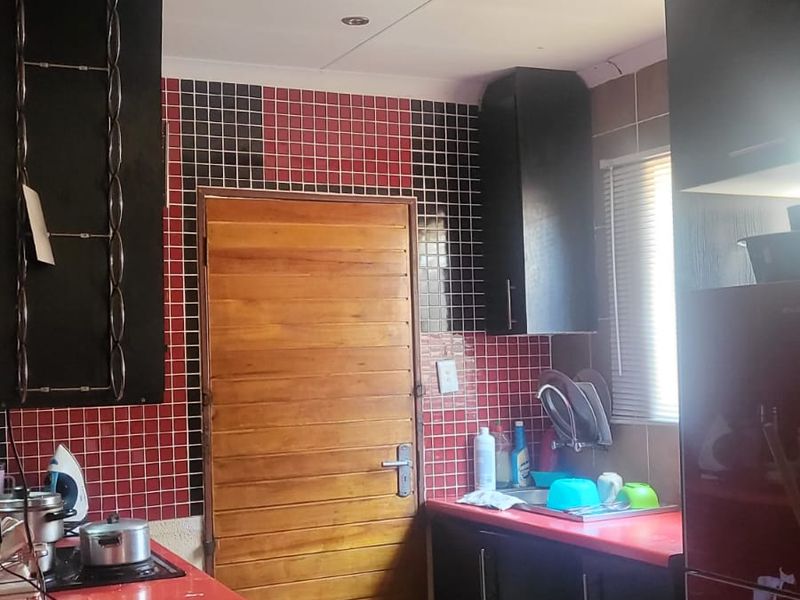 A compact kitchen featuring black cabinetry, red countertops, and a distinctive red and black tiled backsplash with integrated sink and hob.
