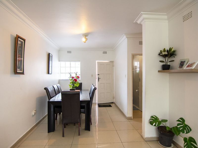 A bright dining area featuring neutral tiled flooring, crown molding, and direct access to the entrance and adjacent utility space.
