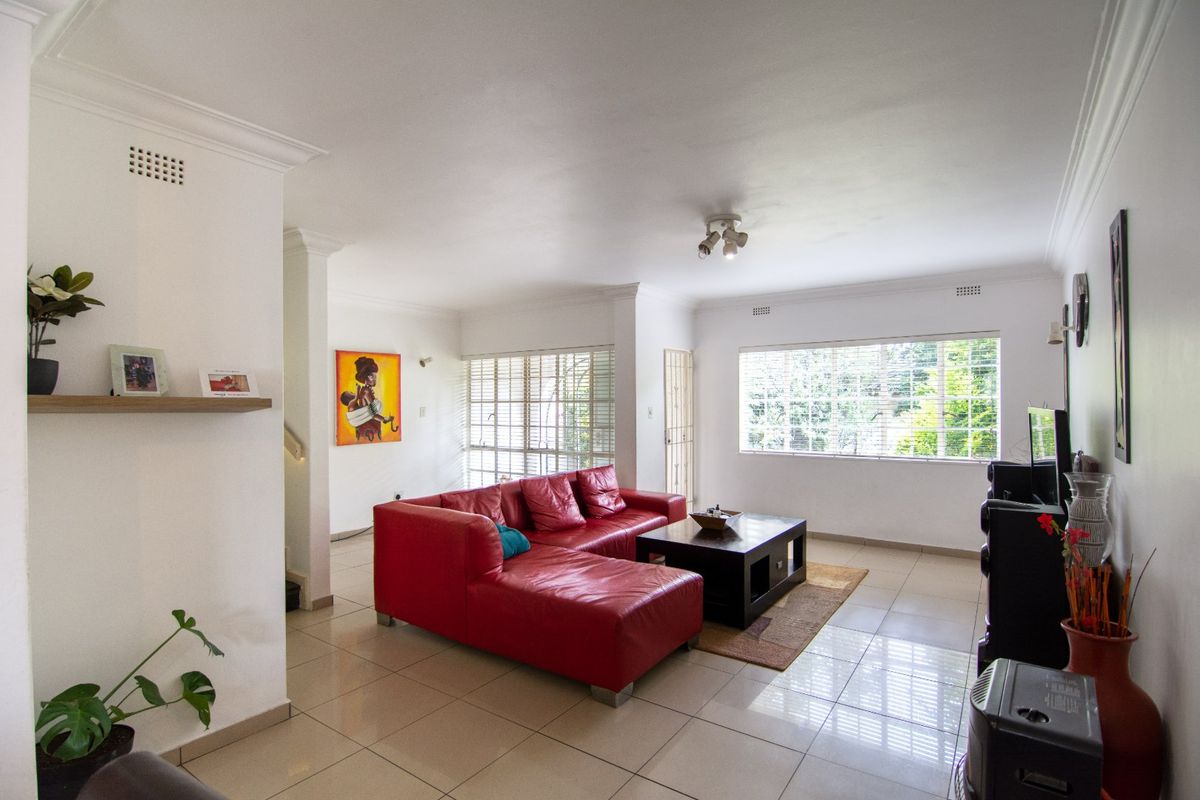 Spacious living room featuring neutral tiled flooring, decorative cornicing, and large windows with venetian blinds, providing ample natural light.