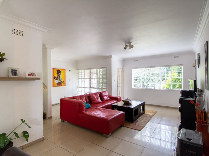 Spacious living room featuring neutral tiled flooring, decorative cornicing, and large windows with venetian blinds, providing ample natural light.