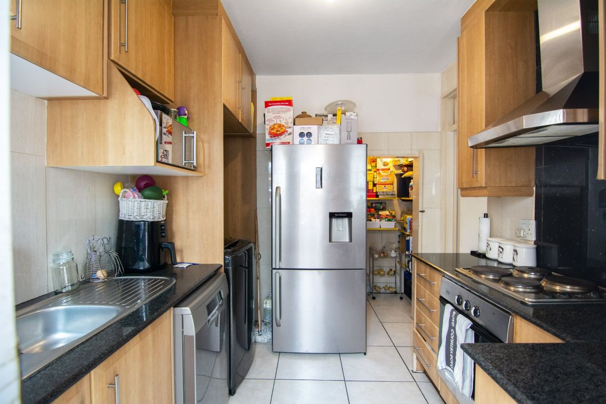Functional kitchen featuring light wood cabinetry, granite countertops, stainless steel appliances, and an adjoining scullery area with tiled flooring throughout.