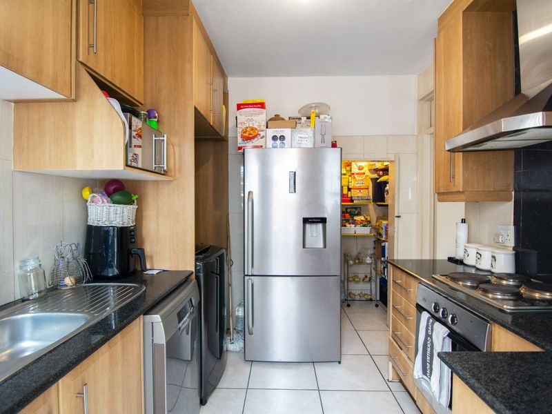 Functional kitchen featuring light wood cabinetry, granite countertops, stainless steel appliances, and an adjoining scullery area with tiled flooring throughout.