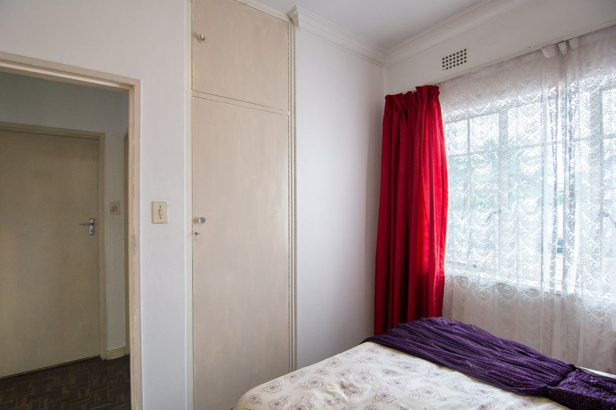 A bedroom featuring a built-in cupboard, cornice detailing, and a window with ventilation grille.