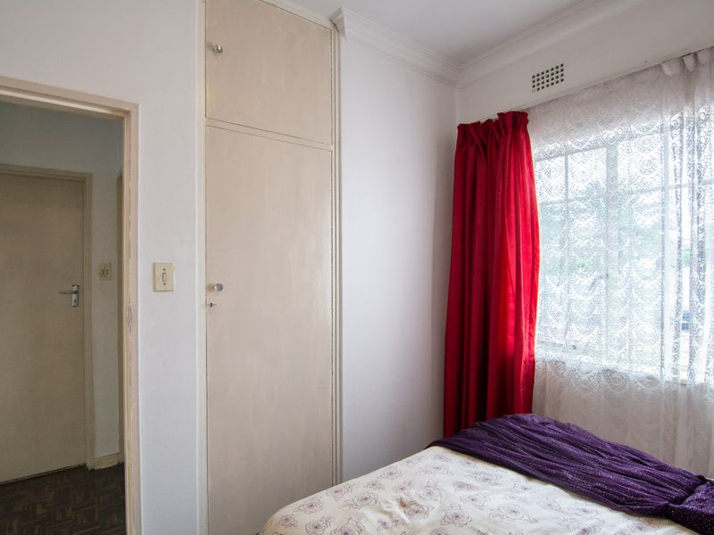 A bedroom featuring a built-in cupboard, cornice detailing, and a window with ventilation grille.