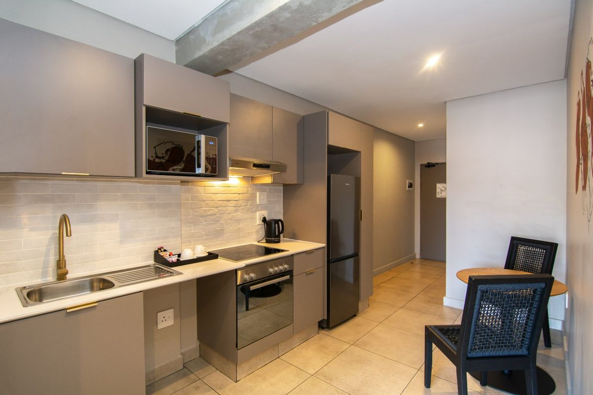 Modern kitchen featuring sleek grey cabinetry, stone countertops, subway tile backsplash, and integrated appliances, seamlessly flowing into the adjacent living area.