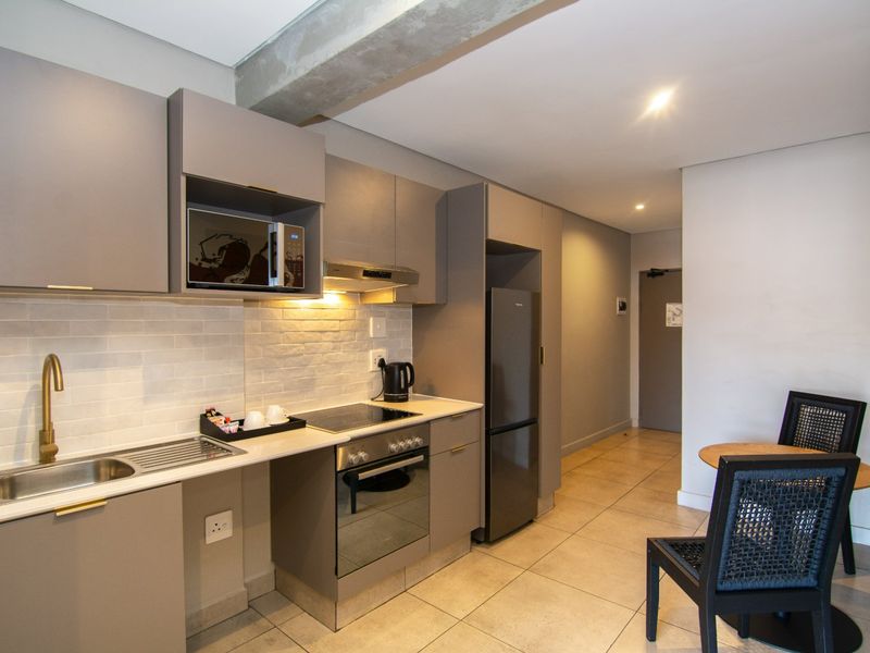 Modern kitchen featuring sleek grey cabinetry, stone countertops, subway tile backsplash, and integrated appliances, seamlessly flowing into the adjacent living area.