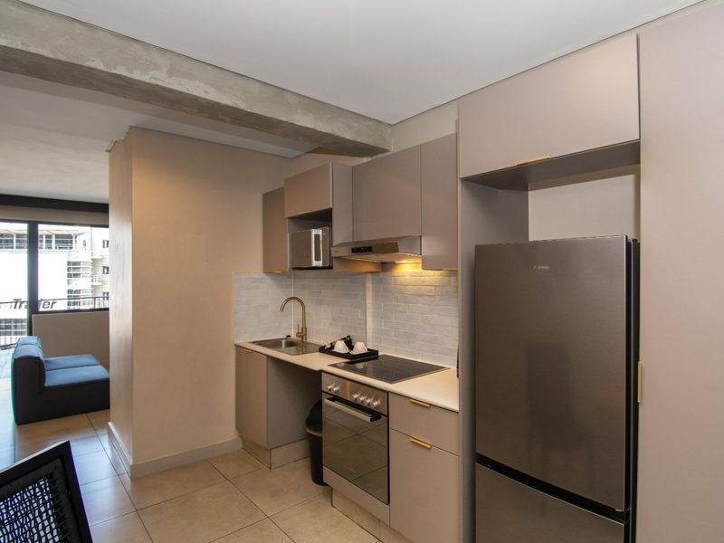 Modern compact kitchen featuring sleek cabinetry, stone countertops, subway tile backsplash, and integrated appliances, including an electric hob and oven.