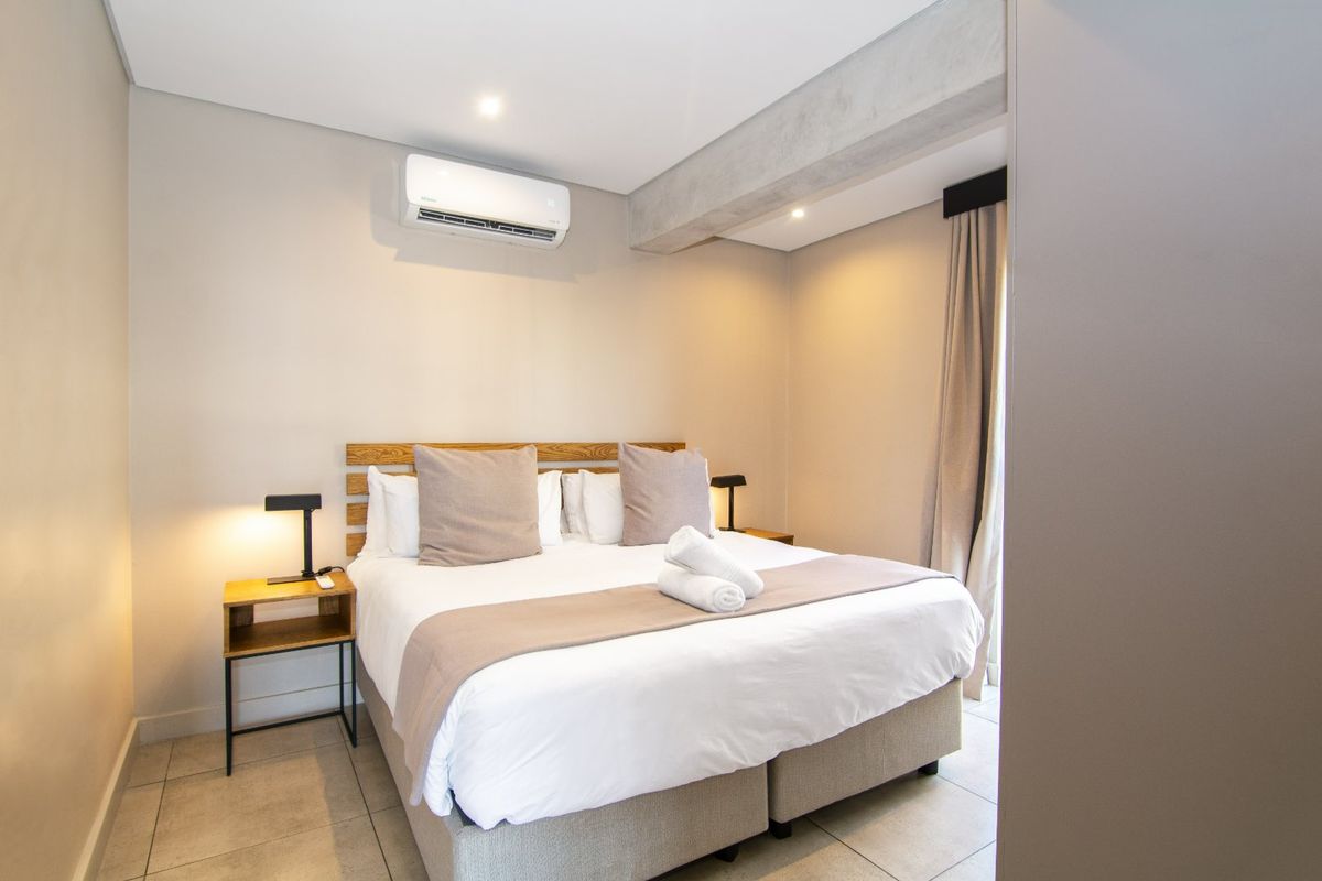 A modern, well-maintained bedroom featuring tiled flooring, an exposed concrete beam, and a wall-mounted air conditioning unit.