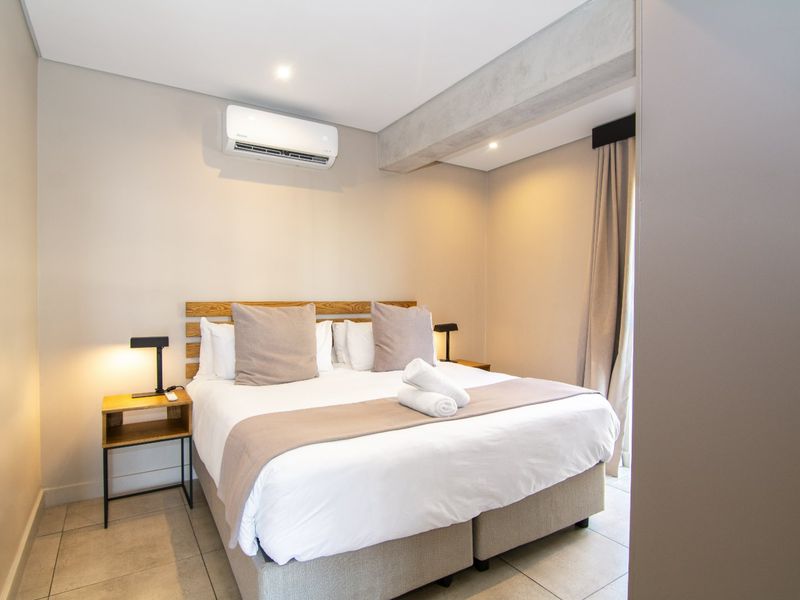 A modern, well-maintained bedroom featuring tiled flooring, an exposed concrete beam, and a wall-mounted air conditioning unit.