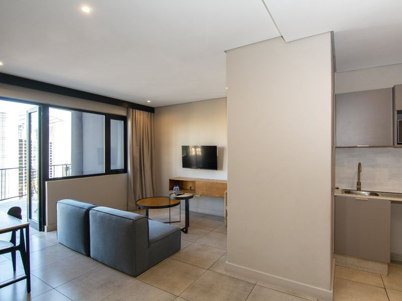 Modern open-plan apartment featuring a compact kitchen area, tiled flooring, and direct access to a private balcony through sliding glass doors.