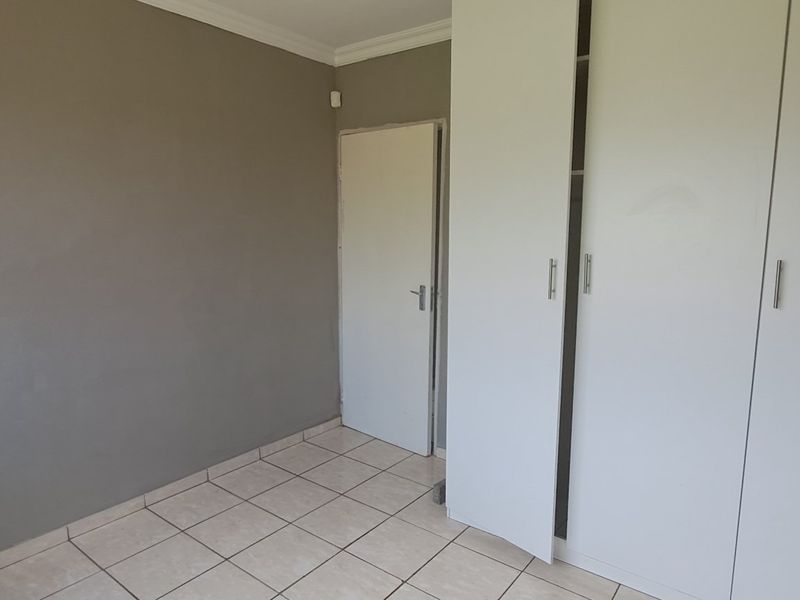 An empty bedroom featuring tiled flooring, neutral grey walls, and built-in white cupboards.