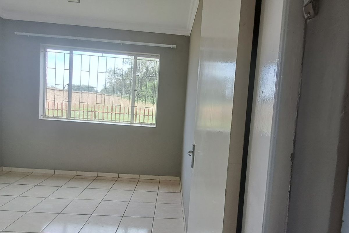 An empty bedroom featuring tiled flooring, neutral grey walls, and a window fitted with security bars.