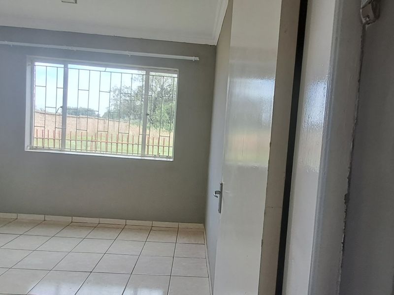 An empty bedroom featuring tiled flooring, neutral grey walls, and a window fitted with security bars.