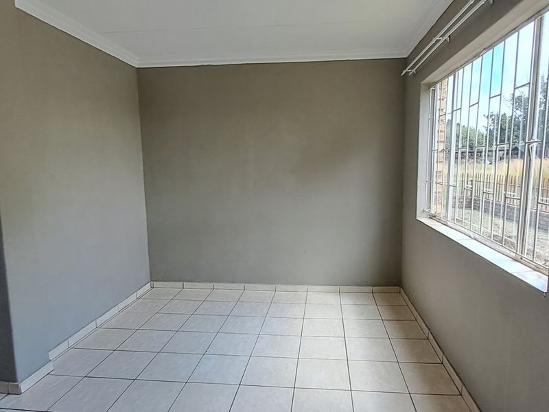 An empty living room featuring neutral grey walls, tiled flooring, and a window fitted with security bars.