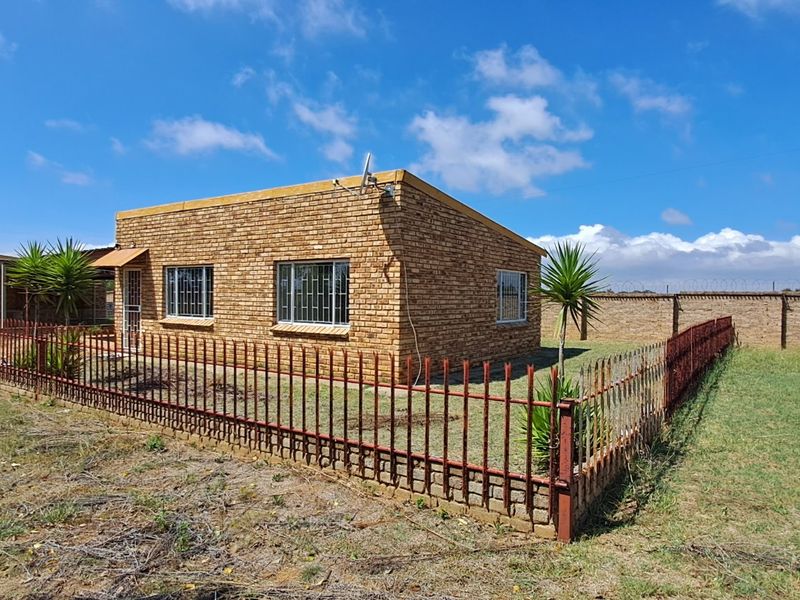 A detached face brick house featuring security bars on windows, enclosed by a perimeter wall and metal fencing on a large plot.