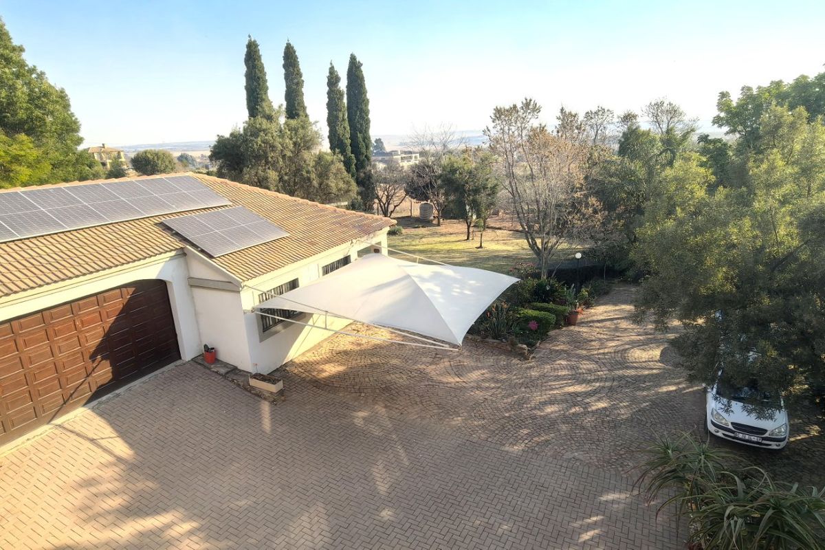 Aerial view of the property featuring a paved driveway, garage, and roof-mounted solar panels set within a landscaped garden.