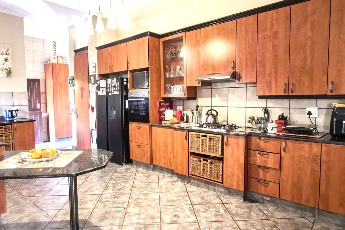 Spacious kitchen featuring wood-finish cabinetry, granite countertops, a gas hob, and integrated appliances with tiled flooring throughout.