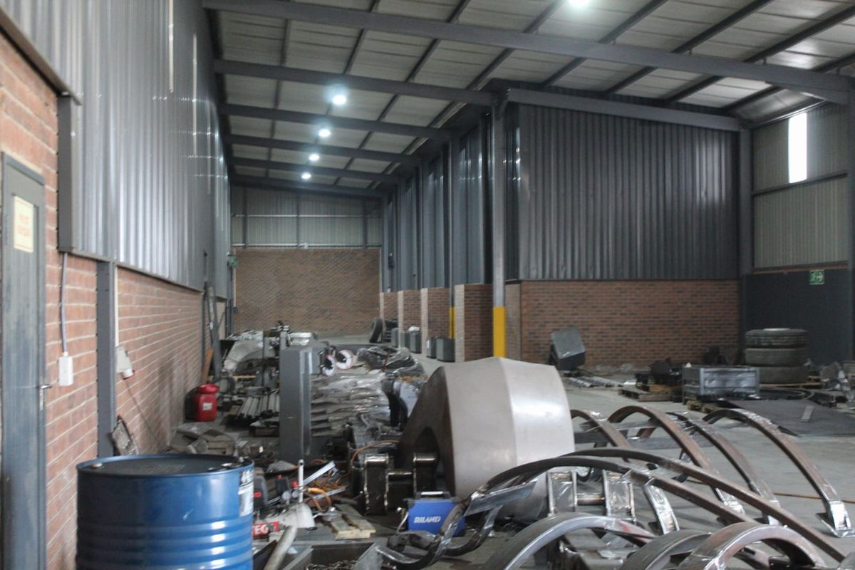 Spacious industrial warehouse unit featuring exposed steel roof trusses, corrugated metal wall cladding, face brick lower walls, and durable concrete flooring.