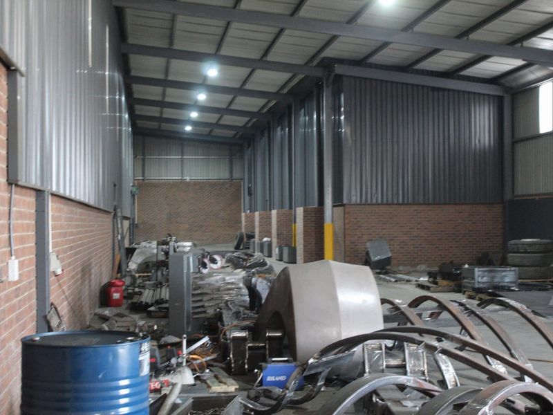 Spacious industrial warehouse unit featuring exposed steel roof trusses, corrugated metal wall cladding, face brick lower walls, and durable concrete flooring.
