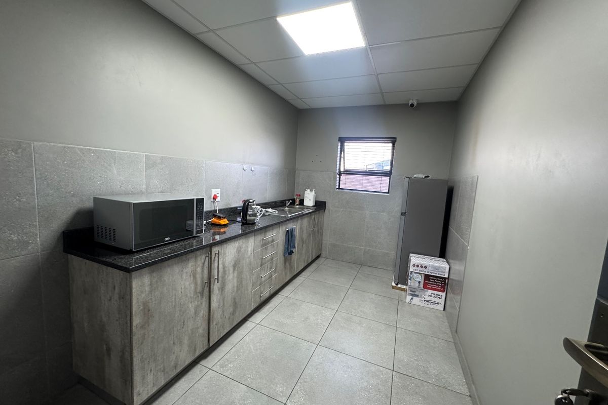 A functional industrial-style kitchenette featuring granite countertops, modern cabinetry, tiled finishes, and a drop ceiling with integrated lighting.
