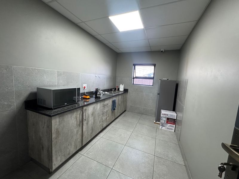 A functional industrial-style kitchenette featuring granite countertops, modern cabinetry, tiled finishes, and a drop ceiling with integrated lighting.