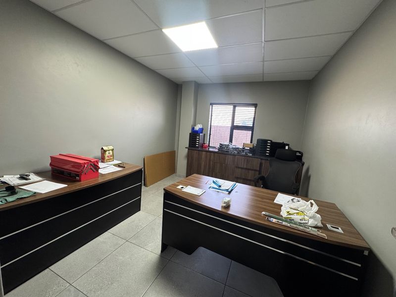 A functional office space featuring tiled flooring, a suspended ceiling with recessed lighting, and built-in storage cabinetry.