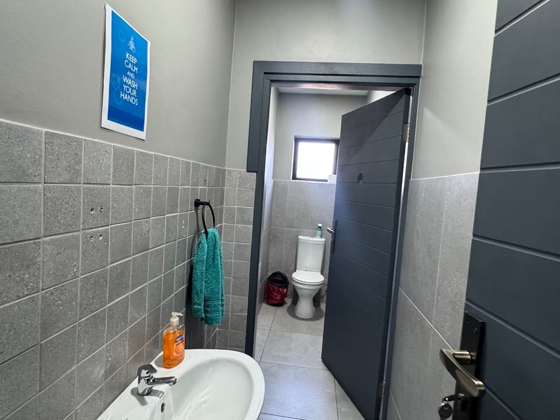 A functional bathroom featuring a pedestal washbasin, tiled walls, and a separate toilet area with modern grey door finishes.