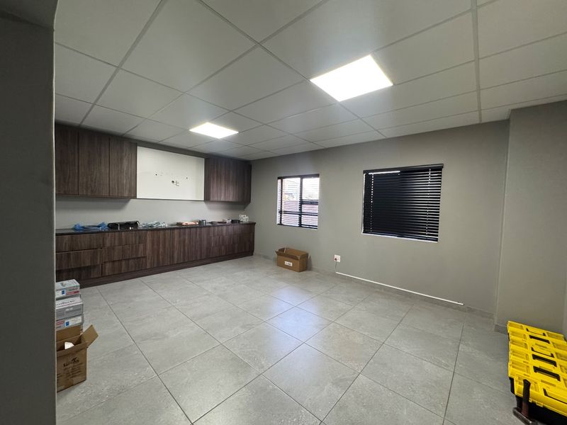 A clean, modern office space featuring neutral grey tiled floors, built-in dark wood cabinetry, and bright recessed panel lighting.