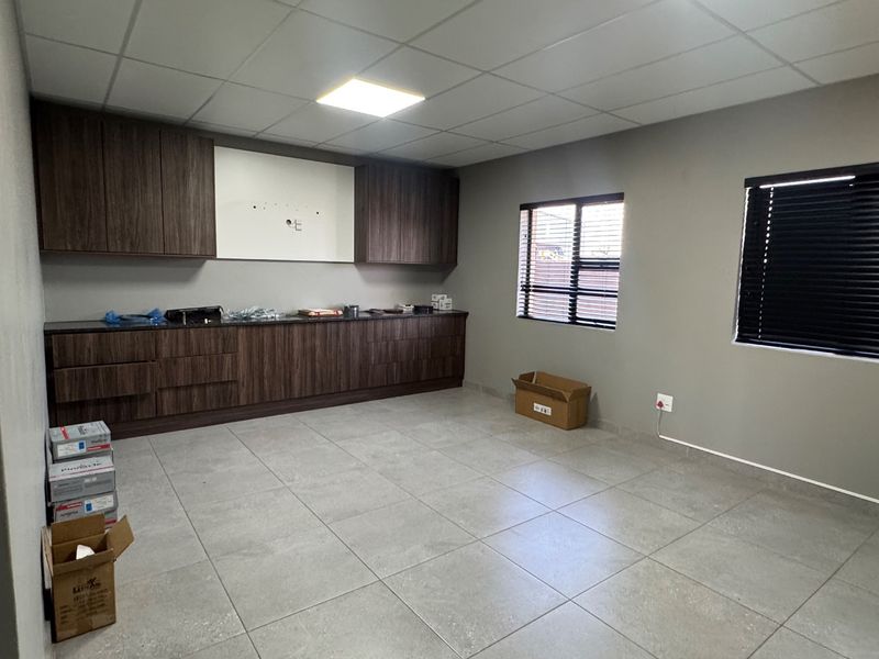 A clean, modern kitchen area featuring dark wood-grain cabinetry, stone-look floor tiles, and a drop ceiling with integrated lighting.