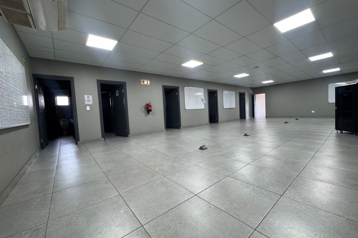 Spacious, open-plan industrial office area featuring tiled flooring, suspended ceilings with recessed lighting, and multiple access points to adjacent rooms.