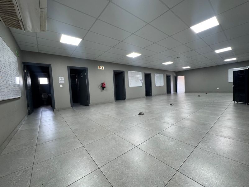 Spacious, open-plan industrial office area featuring tiled flooring, suspended ceilings with recessed lighting, and multiple access points to adjacent rooms.