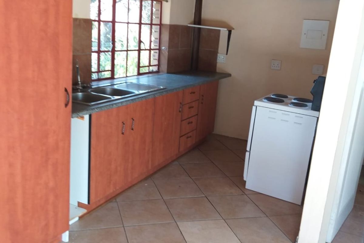 A rustic kitchen featuring a traditional thatched roof with exposed timber rafters, laminate cabinetry, double basin sink, and tiled flooring.