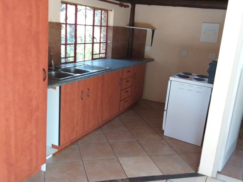 A rustic kitchen featuring a traditional thatched roof with exposed timber rafters, laminate cabinetry, double basin sink, and tiled flooring.