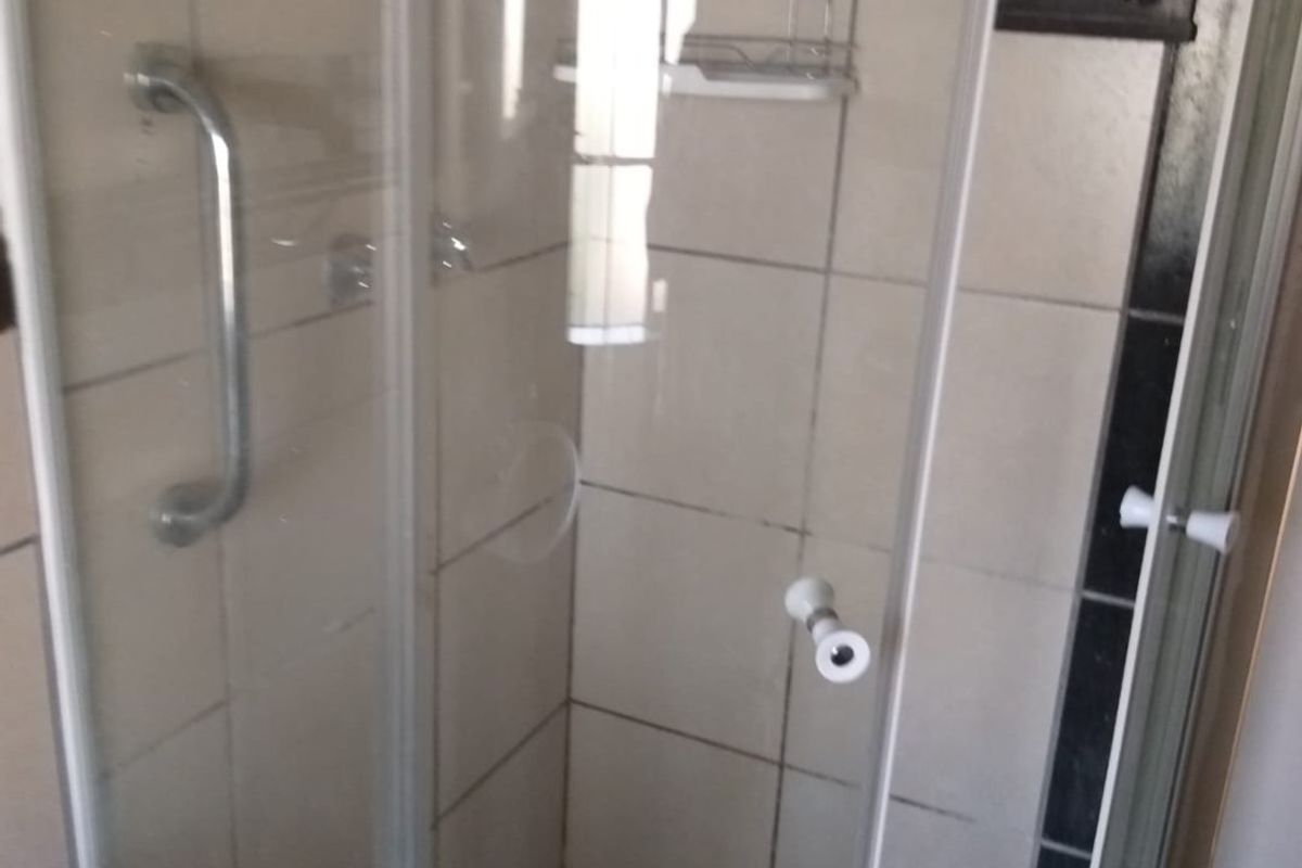 A functional shower enclosure featuring tiled walls, a grab rail, and a tiled floor, requiring some maintenance and cosmetic updates.