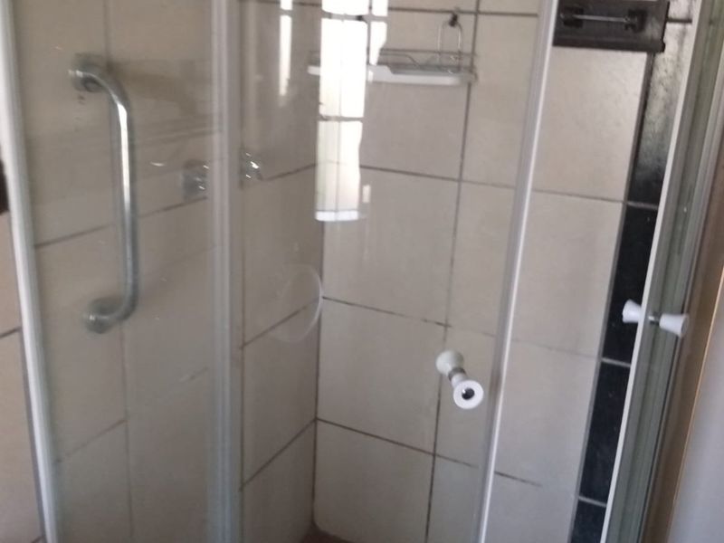 A functional shower enclosure featuring tiled walls, a grab rail, and a tiled floor, requiring some maintenance and cosmetic updates.