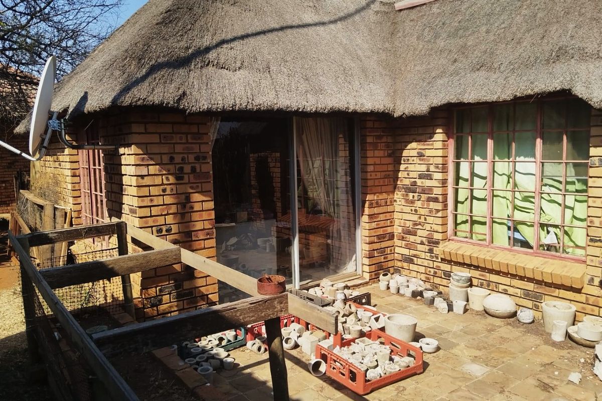 Rear view of a face brick farmhouse featuring a traditional thatch roof, sliding glass doors, and a paved patio area.