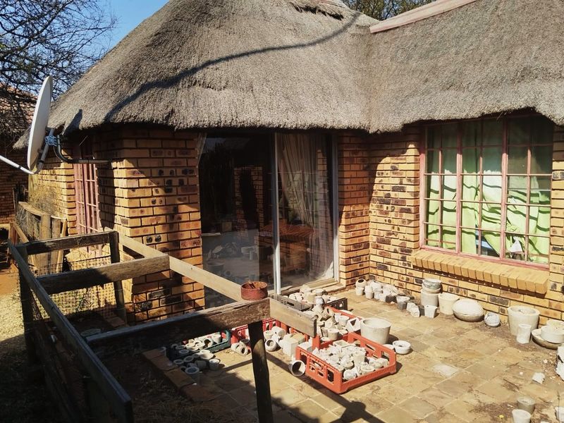 Rear view of a face brick farmhouse featuring a traditional thatch roof, sliding glass doors, and a paved patio area.