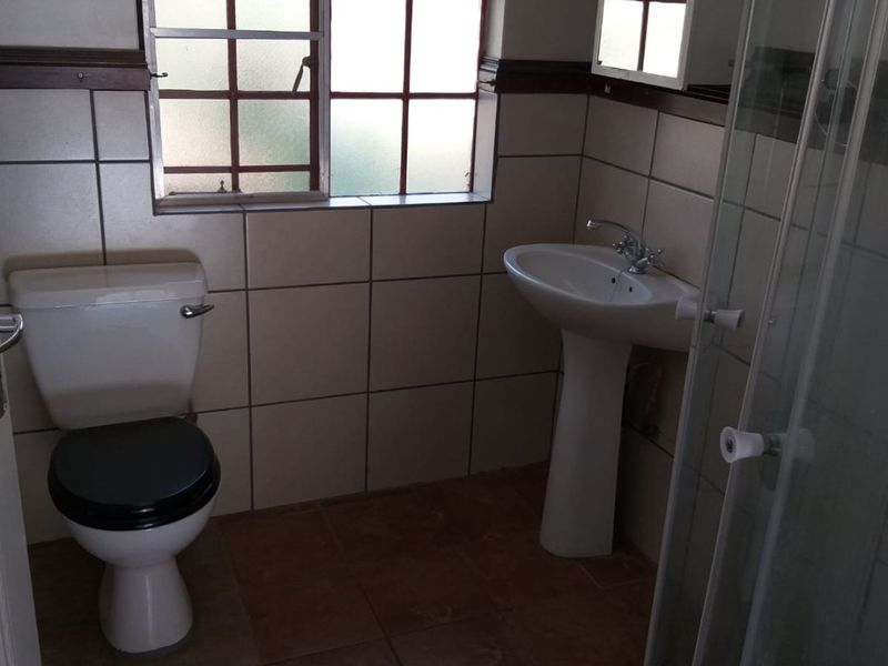 A functional bathroom featuring a pedestal basin, toilet, and shower enclosure with tiled finishes and natural light from a window.