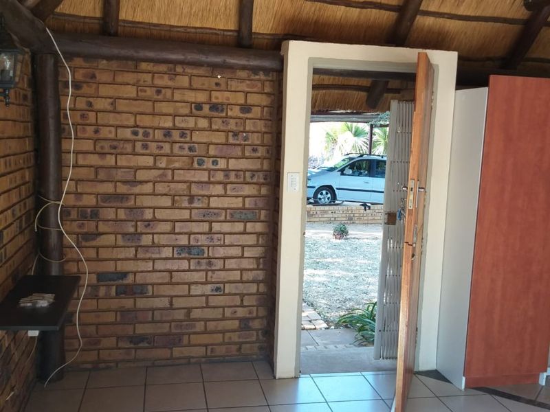 Entrance area featuring rustic exposed brick walls, a traditional thatched roof with timber rafters, and ceramic tiled flooring.