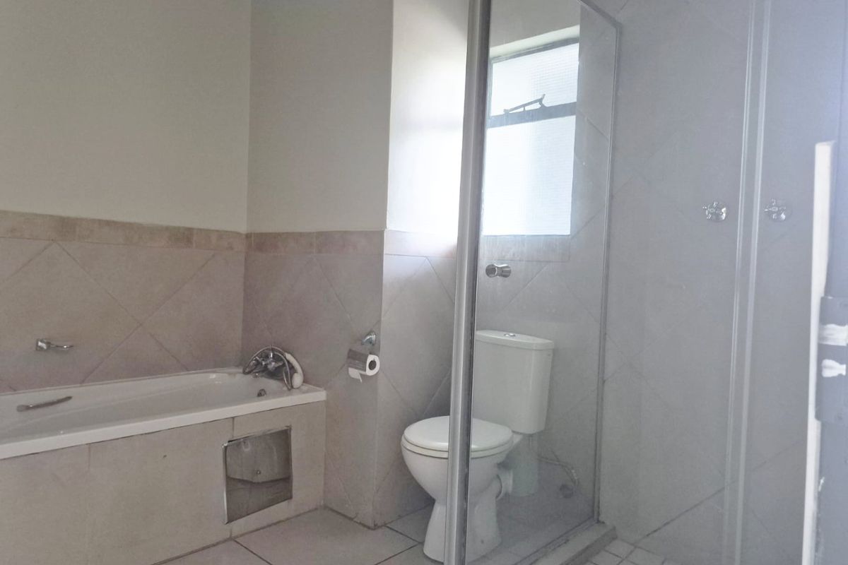 A functional bathroom featuring a bathtub, a separate shower enclosure, and a toilet, finished with neutral wall and floor tiling.