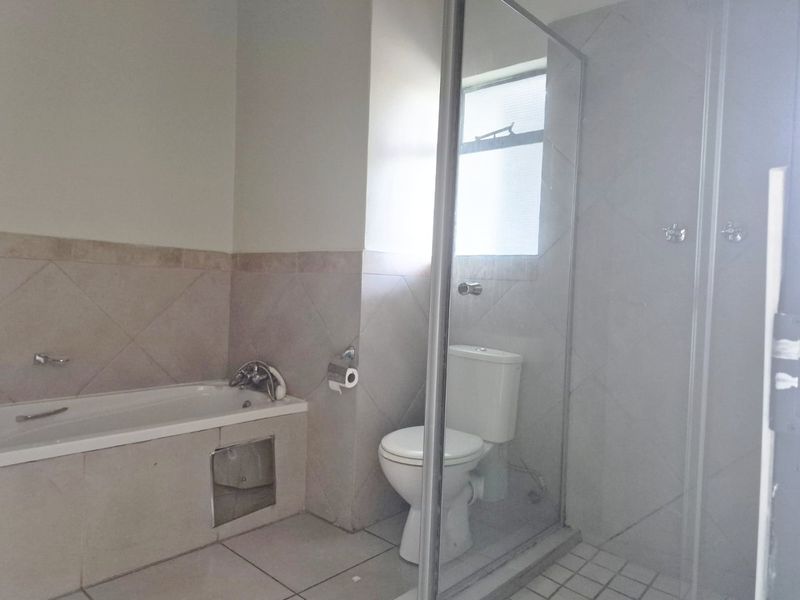A functional bathroom featuring a bathtub, a separate shower enclosure, and a toilet, finished with neutral wall and floor tiling.