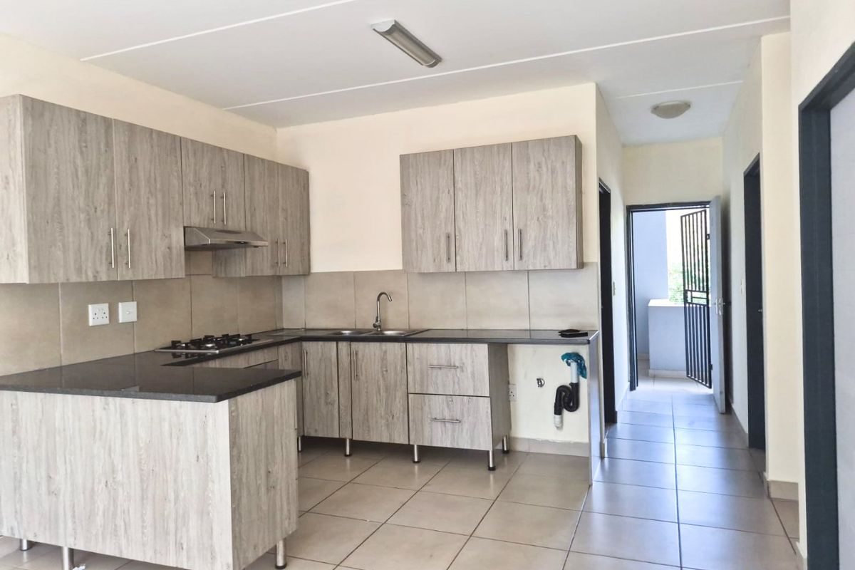 Modern kitchen featuring light wood-grain cabinetry, dark stone countertops, gas hob, extractor fan, and tiled flooring, with an open-plan layout leading to a balcony.