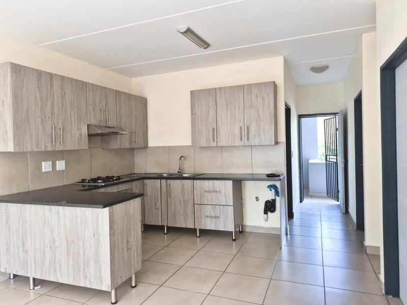 Modern kitchen featuring light wood-grain cabinetry, dark stone countertops, gas hob, extractor fan, and tiled flooring, with an open-plan layout leading to a balcony.