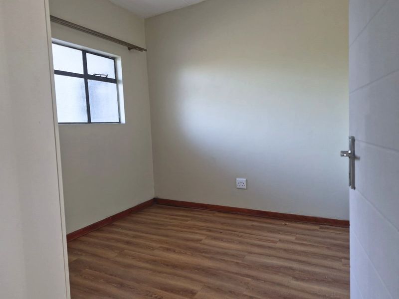 An empty bedroom featuring laminate flooring, neutral walls, and a window, providing a blank canvas for personalization.