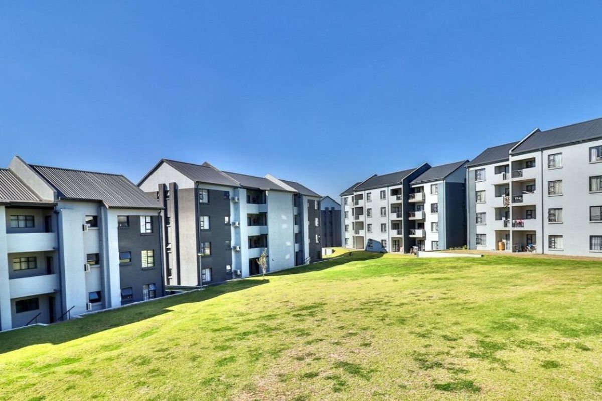 A view of the rear elevation of a modern apartment complex featuring multi-story buildings with balconies and a well-maintained communal lawn area.