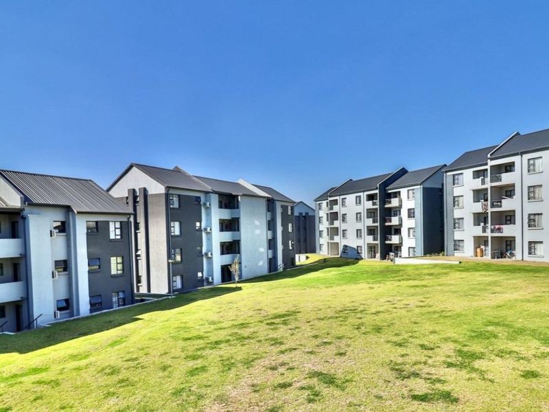 A view of the rear elevation of a modern apartment complex featuring multi-story buildings with balconies and a well-maintained communal lawn area.