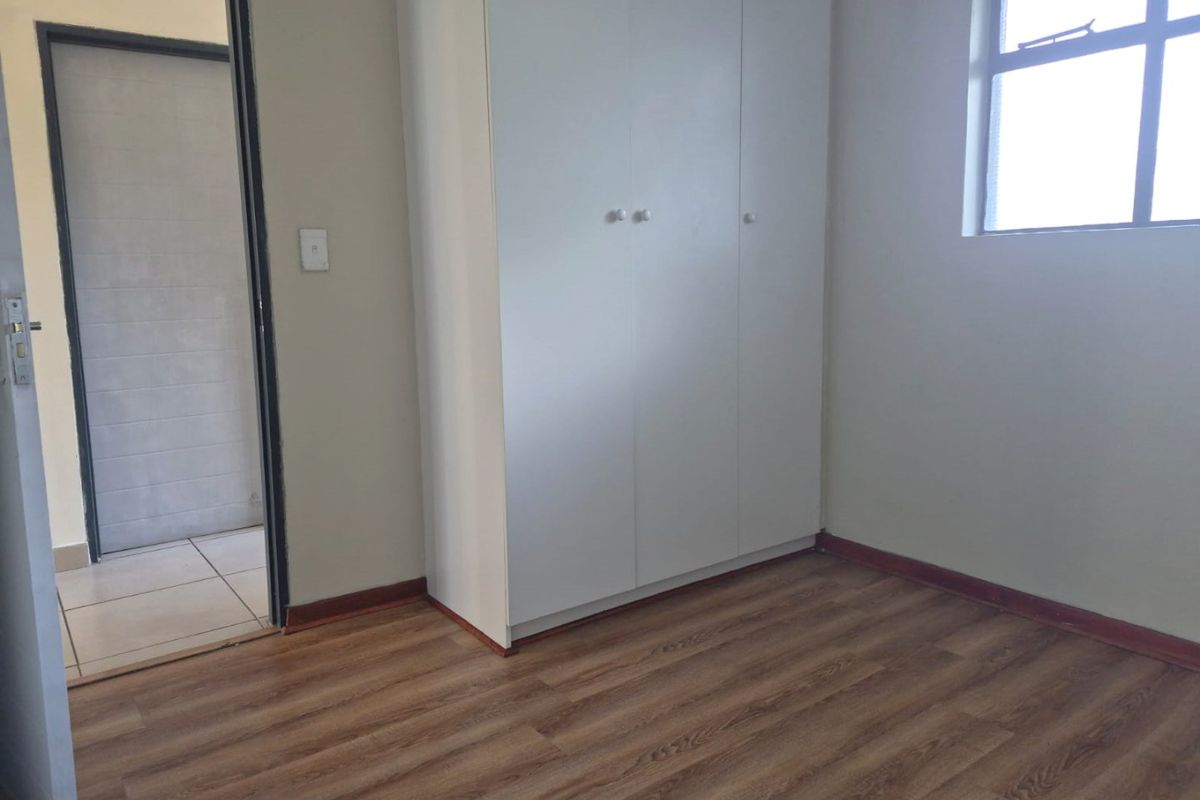 A clean, empty bedroom featuring laminate flooring, a built-in wardrobe, and neutral wall finishes, providing a versatile space ready for personalization.
