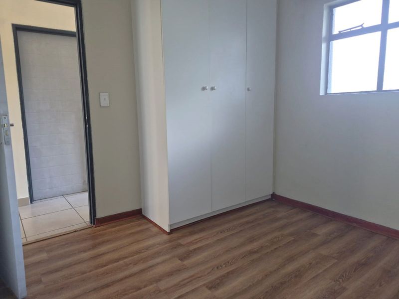 A clean, empty bedroom featuring laminate flooring, a built-in wardrobe, and neutral wall finishes, providing a versatile space ready for personalization.